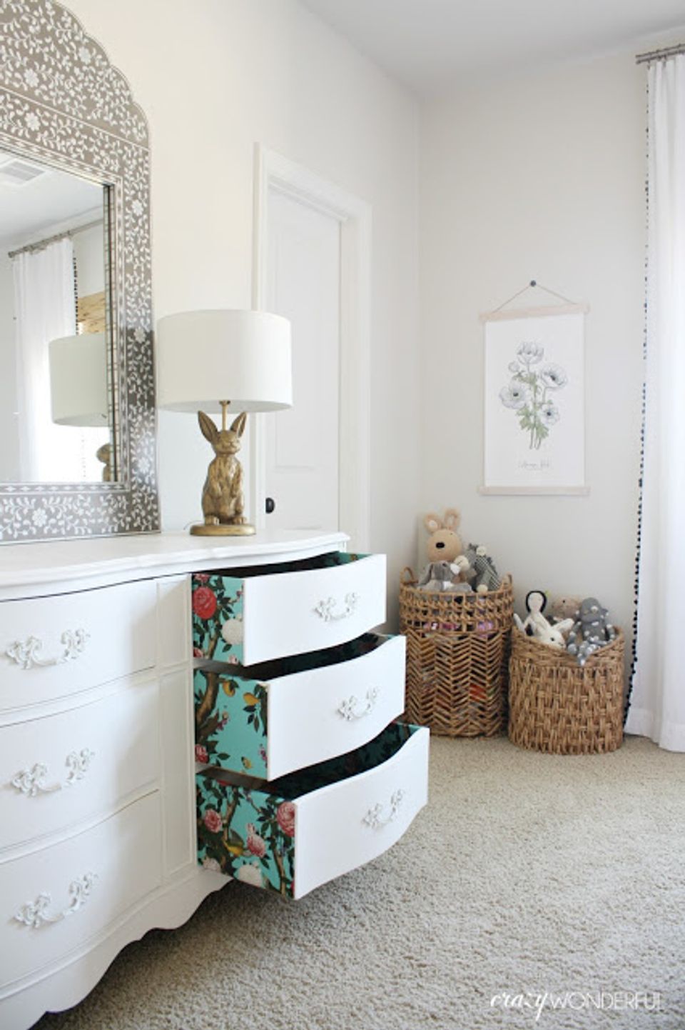 Feminine nursery with floral peel-and-stick accents on dresser drawers and botanical mirror frame