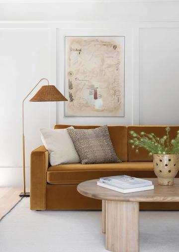Warm minimalist seating area featuring caramel leather sofa, brass arc lamp, light wood table, and neutral textiles in calm palette.