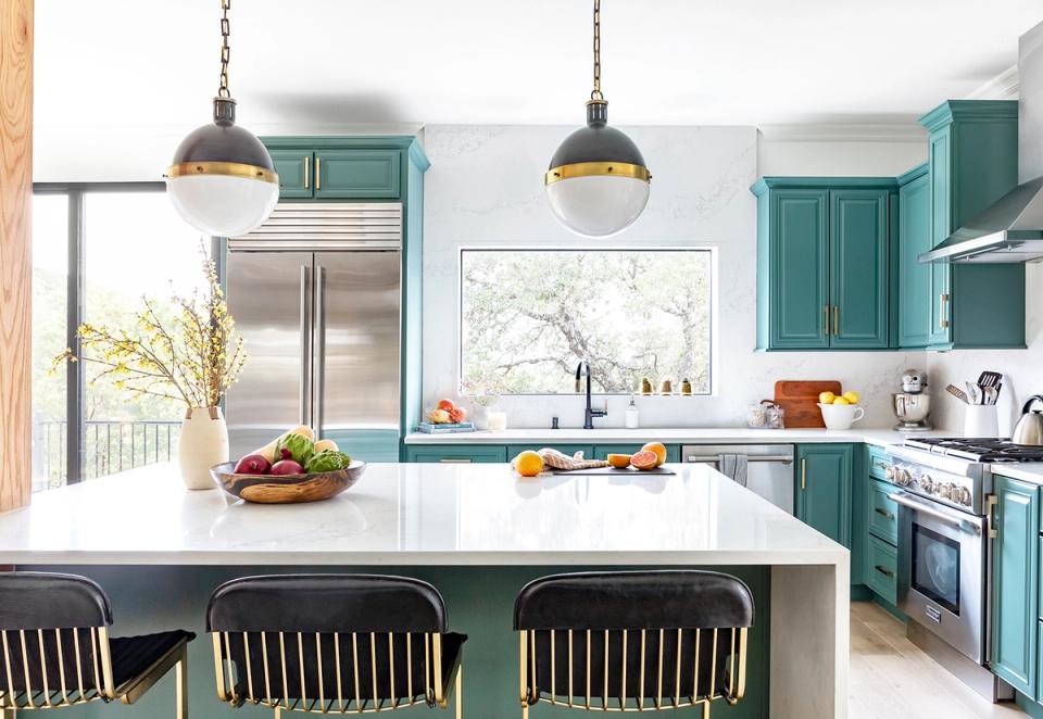 Modern farmhouse kitchen with teal cabinetry, white marble island, and warm brass pendant lights creating a bright, airy aesthetic.
