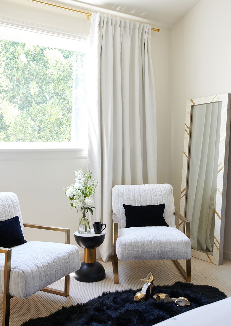 Modern bedroom sitting area with mid-century wooden chairs, brass accents, flowing linen curtains, and minimalist decor