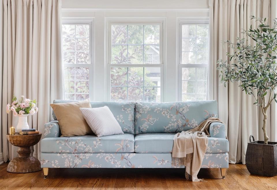 Modern living room with blue floral print sofa, solid and patterned throw pillows in warm neutrals, demonstrating balanced print layering