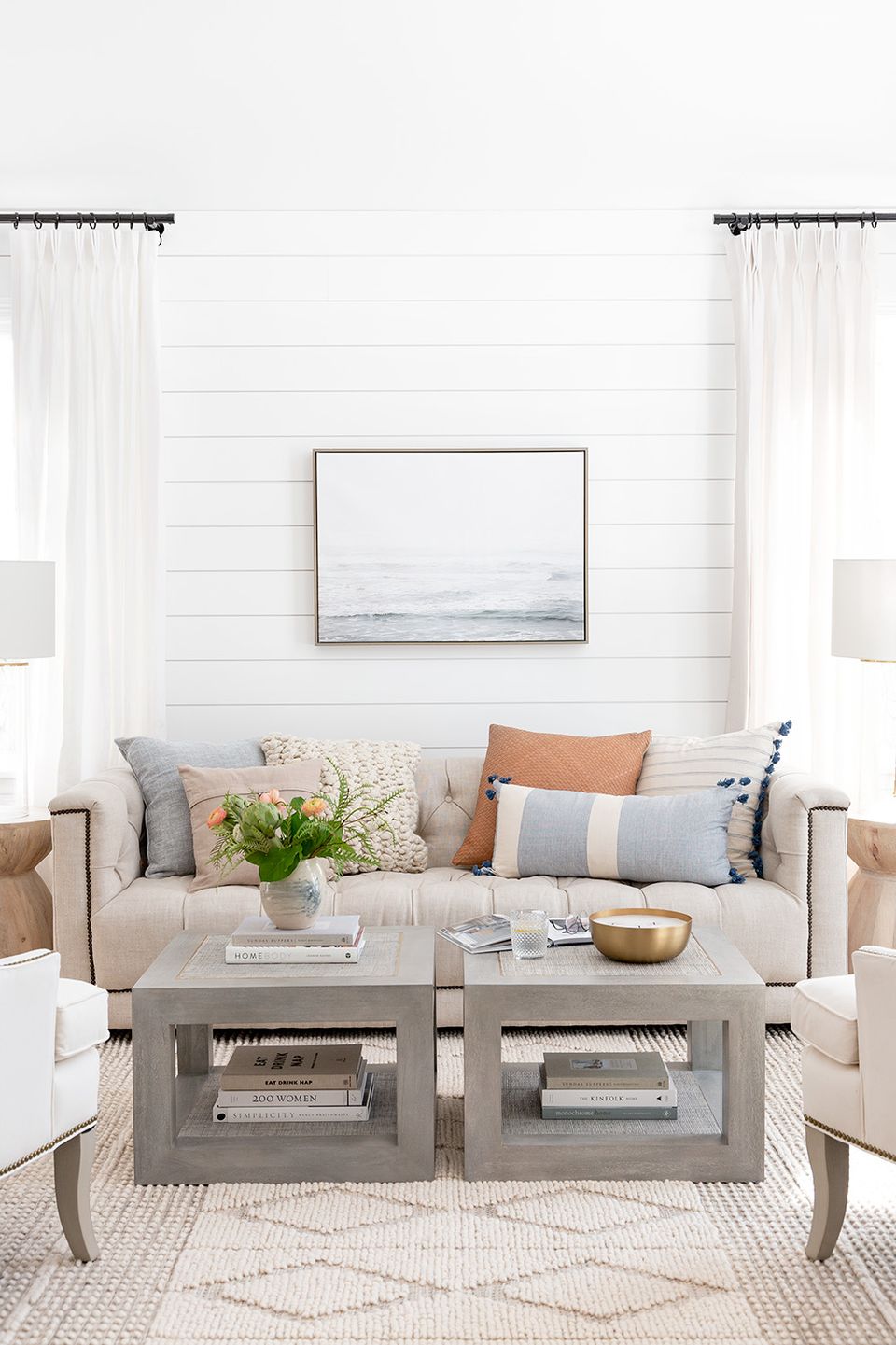 Coastal-inspired living room featuring white shiplap walls, beige upholstery, warm wood accents, and soft neutral palette with pops of tan