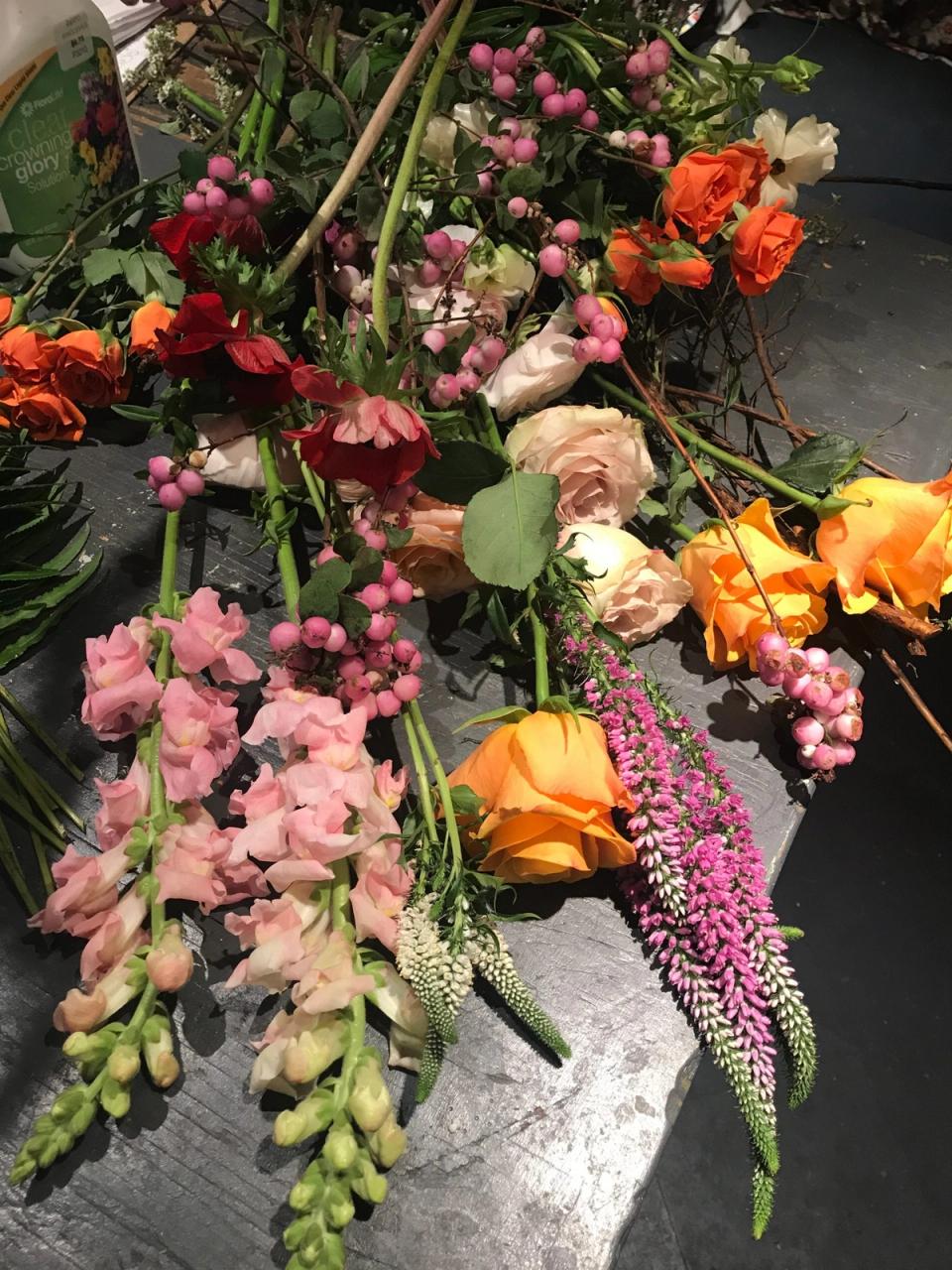 Vibrant mixed flower arrangement with pink, orange, and coral blooms in romantic garden style on dark surface.