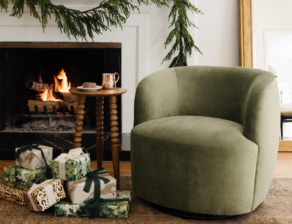 Cozy modern living room with sage green curved chair, fireplace, and festive greenery garland