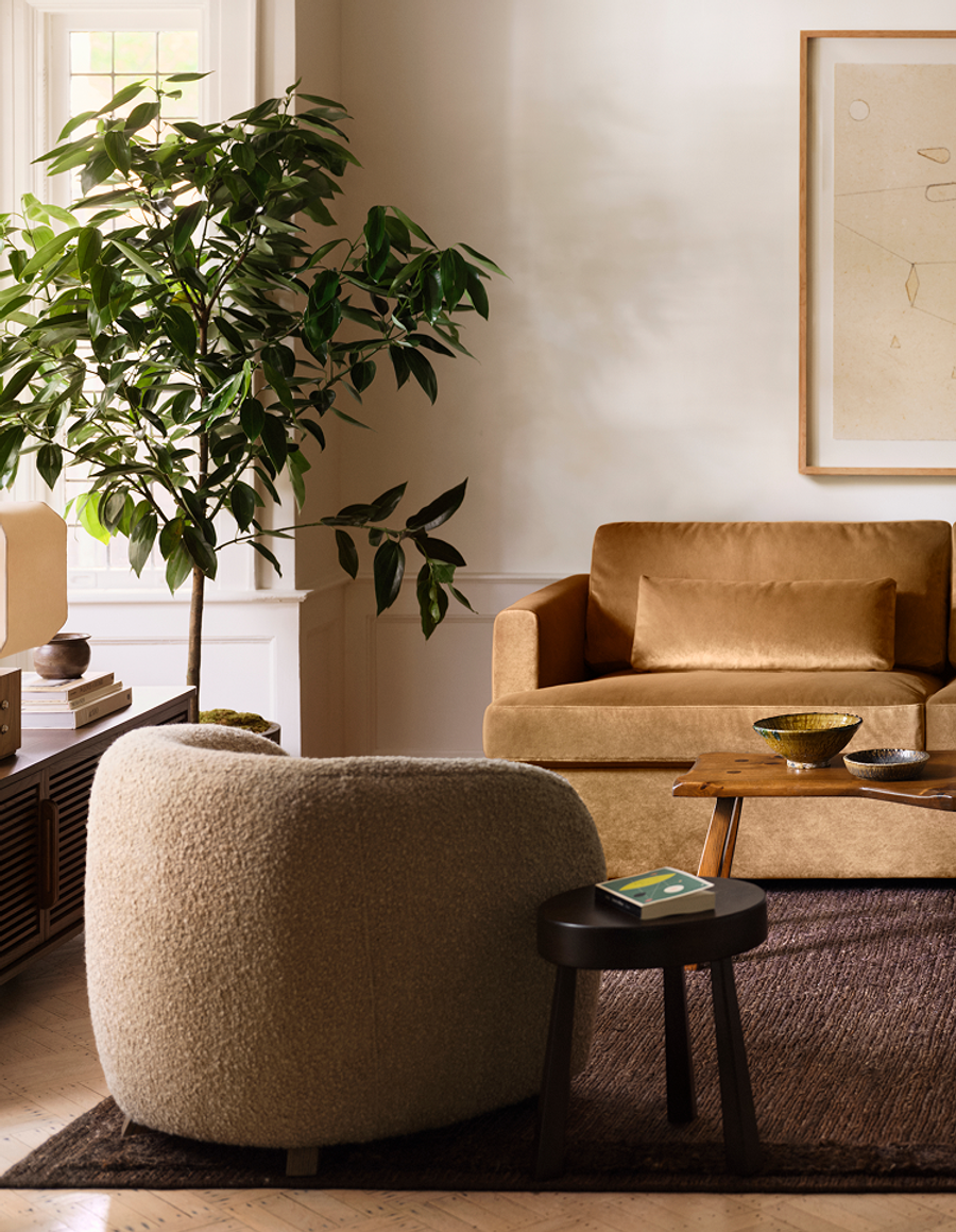 Living room with a gold velvet sofa, boucle swivel chair, and live-edge coffee table on a brown rug.
