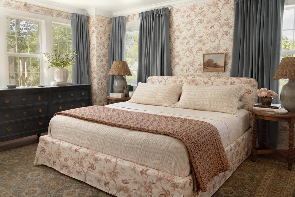 Traditional bedroom with floral wallpaper, cream bedding, gray drapes, and warm wood furnishings creating a classic, elegant aesthetic.