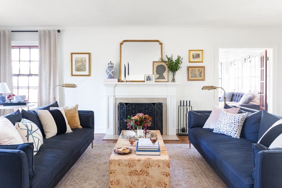 Symmetrical coastal living room with navy sofas, fireplace mantel gallery wall, and warm wood accents