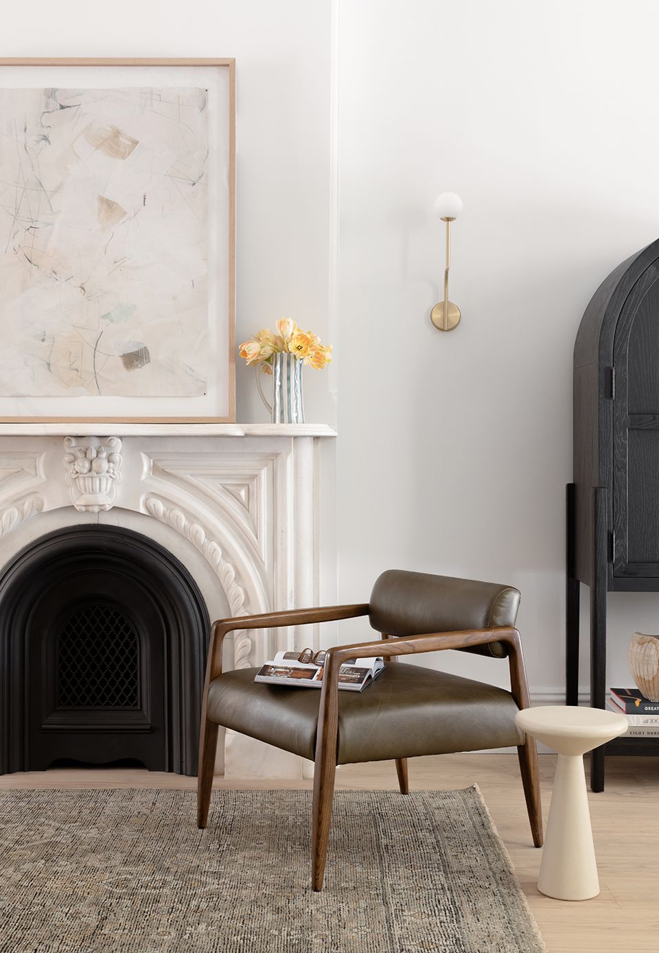 Modern fireplace corner with mid-century leather chair, abstract art, and minimalist styling in warm neutrals and black