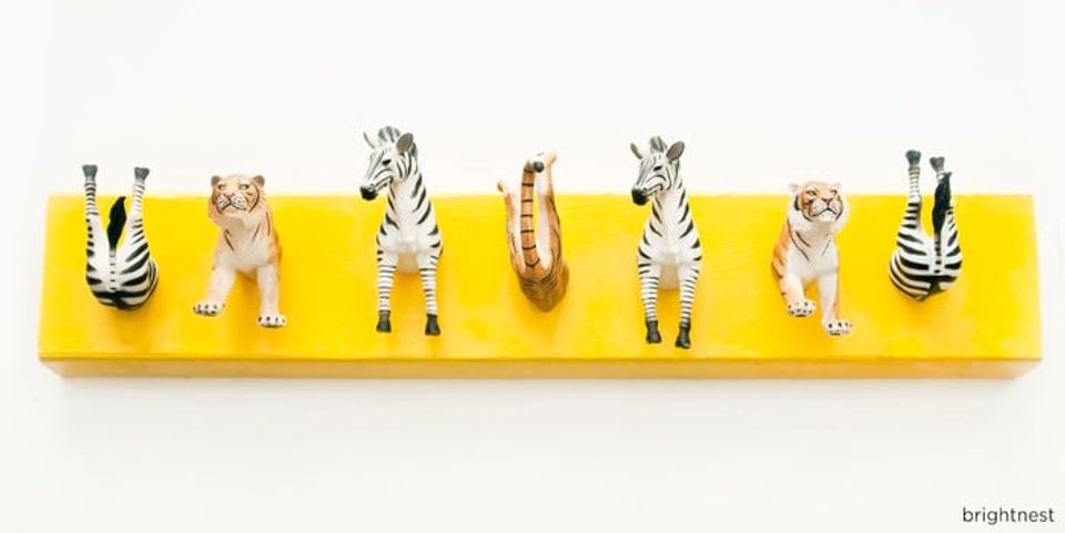 Bright yellow floating shelf with whimsical zebra-striped ceramic figurines, playful maximalist entryway storage