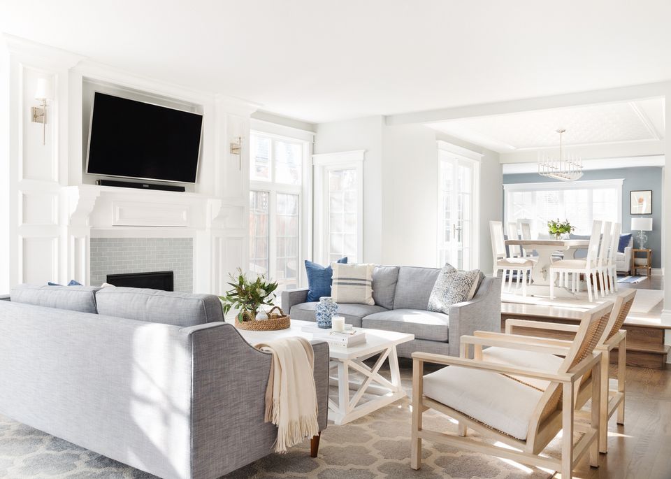 Bright coastal living room with white fireplace, gray upholstered sofa, natural wood accents, and soft neutral palette