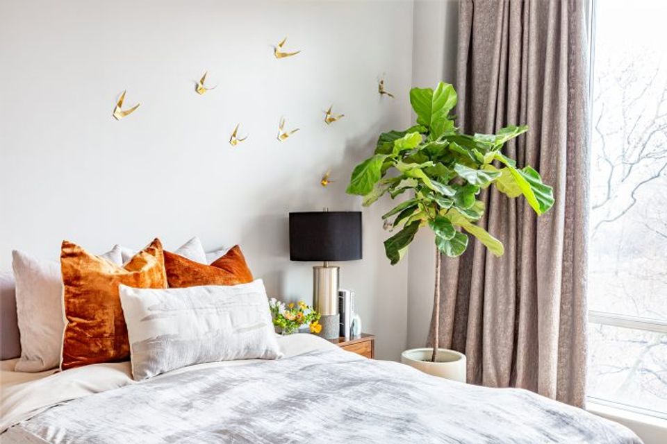 Warm modern bedroom with golden bird wall decals, burnt orange velvet pillows, and lush green plant accent