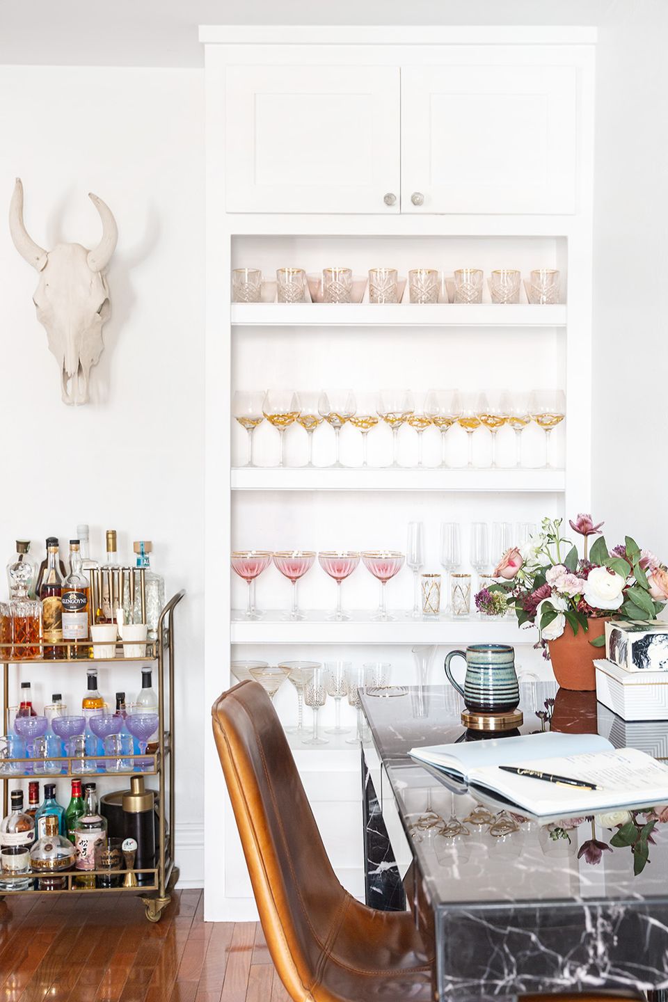 Contemporary glam home office with white shelving, organized bar cart, and marble desk