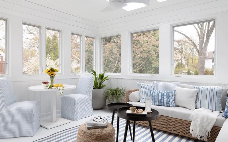 Bright coastal sunroom with white shiplap, blue striped accents, natural wicker, and floor-to-ceiling windows