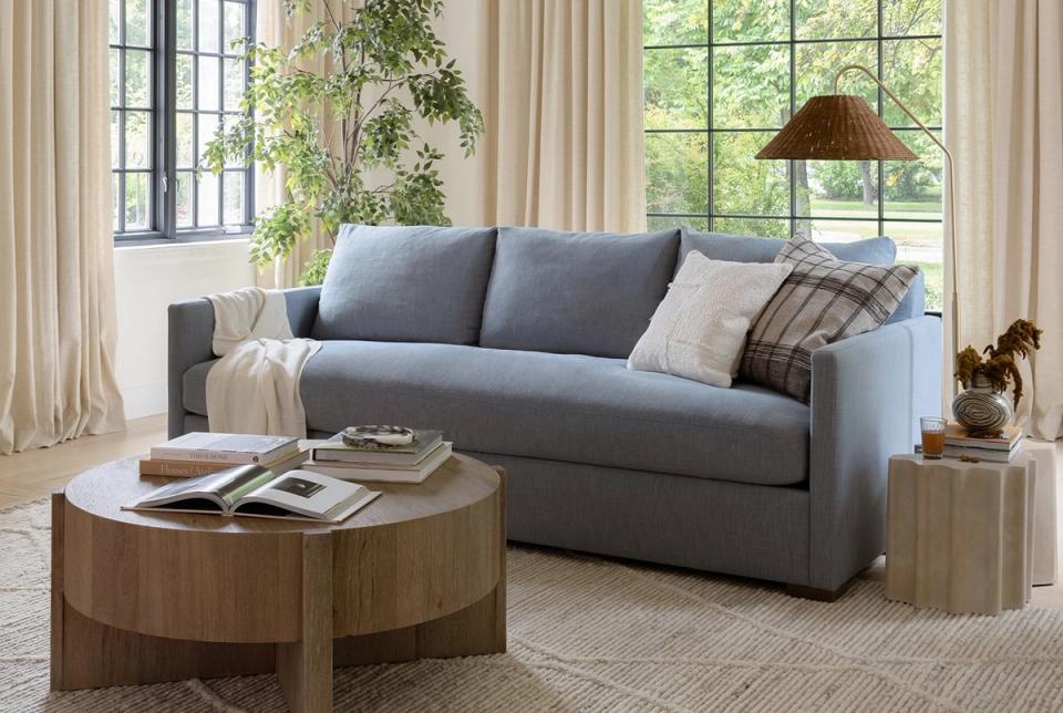 Contemporary farmhouse lounge with slate blue sofa, layered pillows, natural wood table, and soft cream drapery