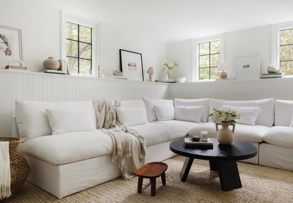 Contemporary coastal living room with cream upholstery, shiplap wall trim, black round coffee table, and layered neutral tones with subtle natural textures