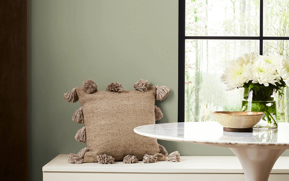 Soft sage green wall with natural wood accents, neutral textiles, and greenery creating a peaceful, contemporary sanctuary