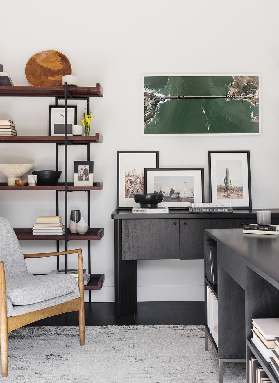 Modern industrial office space with black metal shelving, warm wood accents, and gallery wall framing featuring nature photography and landscape artwork