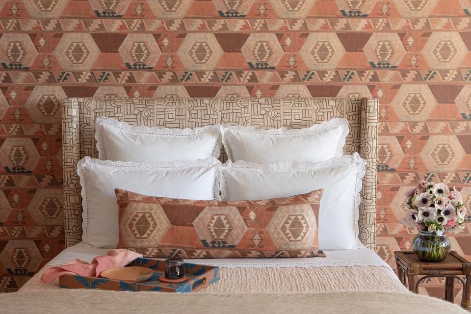 Maximalist bedroom with rust geometric wallpaper, white bedding, and warm earth tones