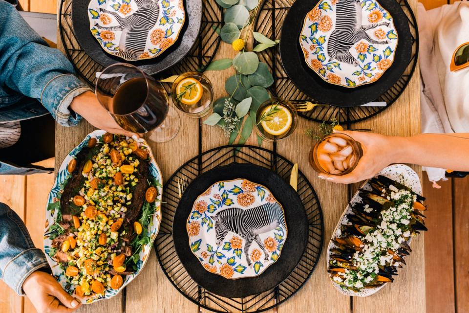 Warm harvest table setting with patterned black plates, golden vegetables, and natural wood surface