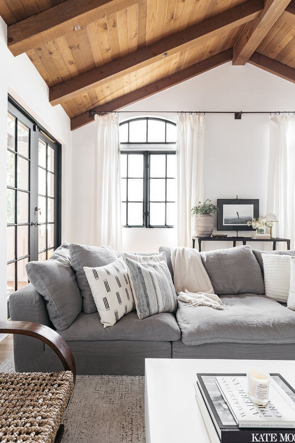 Organic modern living room with exposed wood beams, gray upholstered sofa, and neutral striped pillows under bright natural light