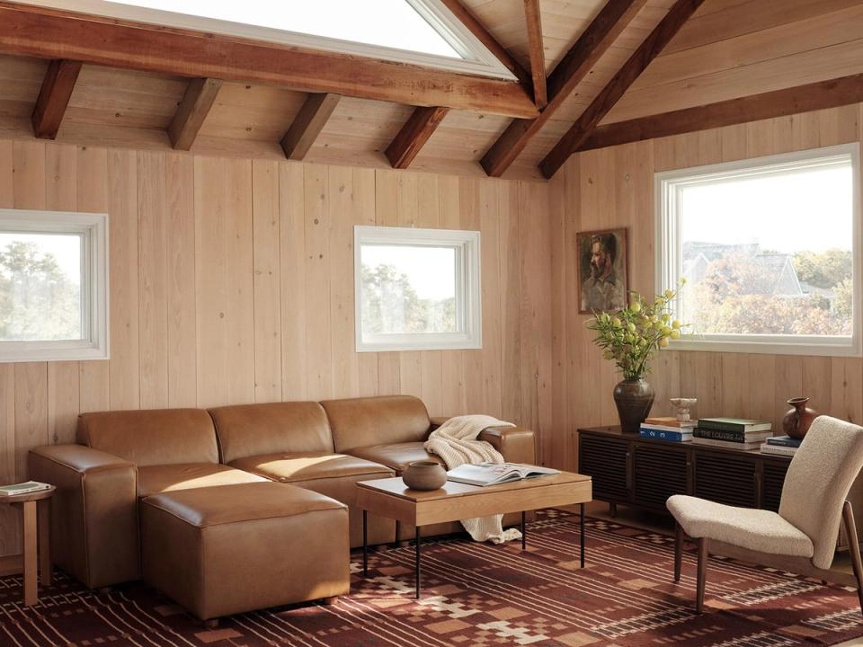 Warm rustic cabin living room with caramel leather sectional, exposed wooden beams, and geometric patterned rug