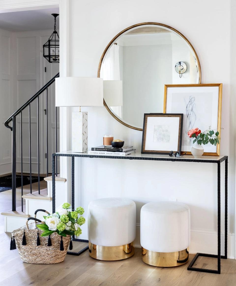 Modern entryway with brass-trimmed round mirror, black console, and neutral upholstered stools