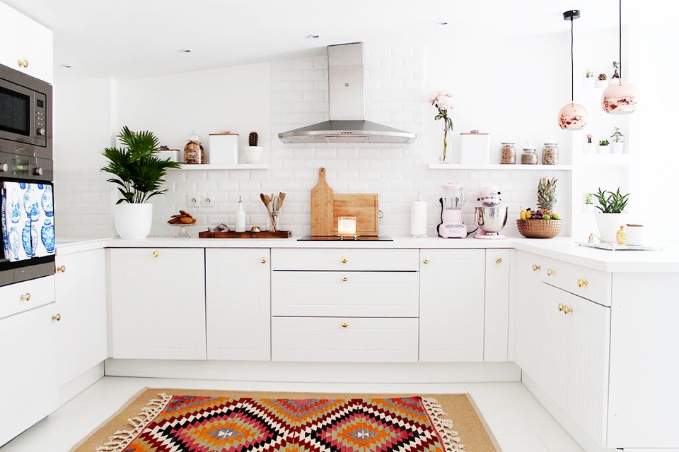 Scandinavian kitchen with white cabinetry, warm wood accents, geometric rug, and botanical touches