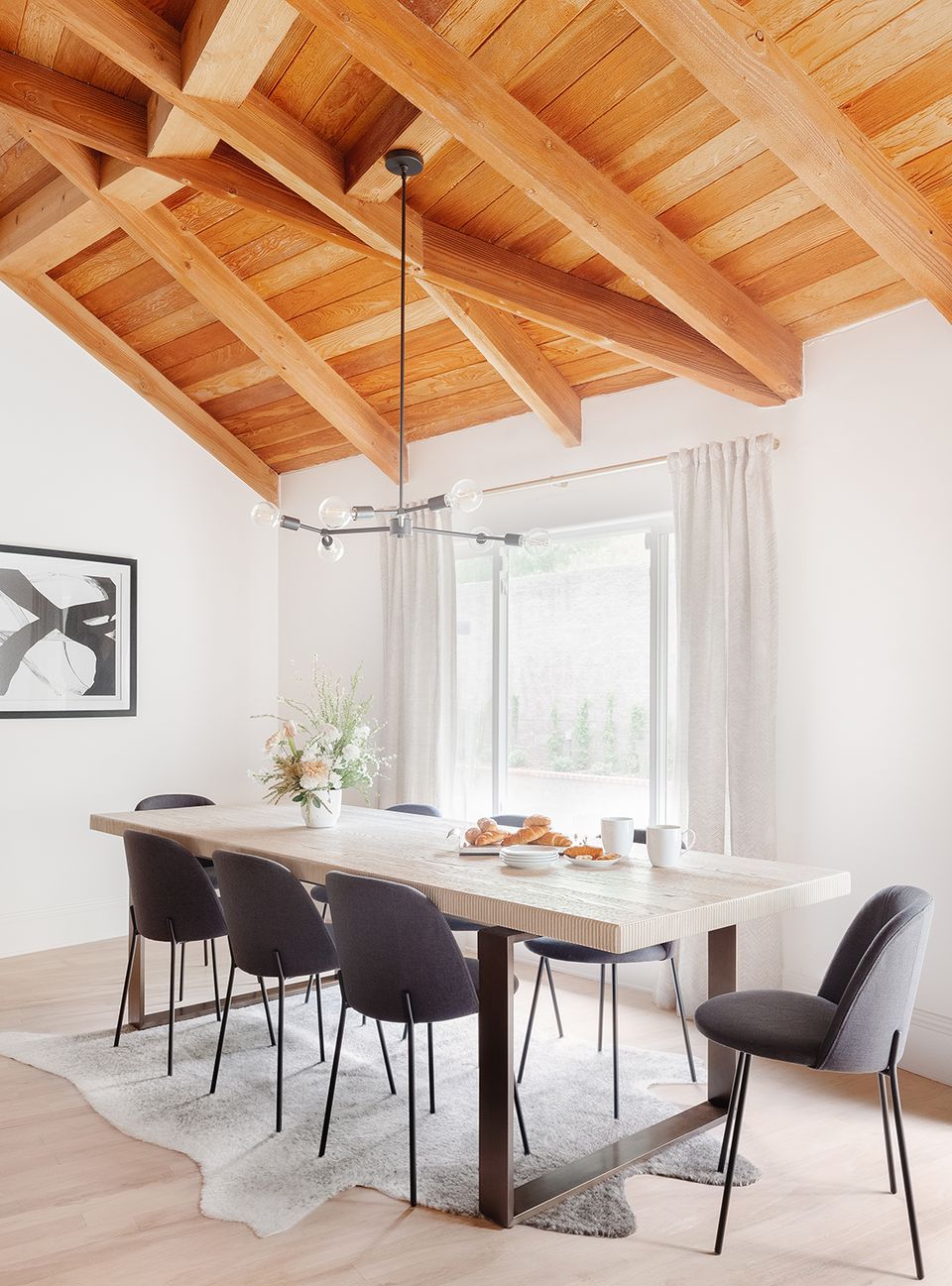 Scandinavian dining space with warm wood ceiling beams, soft white walls, mid-century black chairs, and natural light creating an airy, modern vibe.
