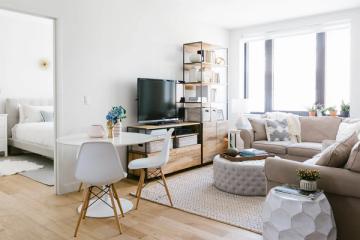 Mid-century modern small living room with TV on wooden stand, light neutral palette, natural wood legs on furniture, and bright airy aesthetic