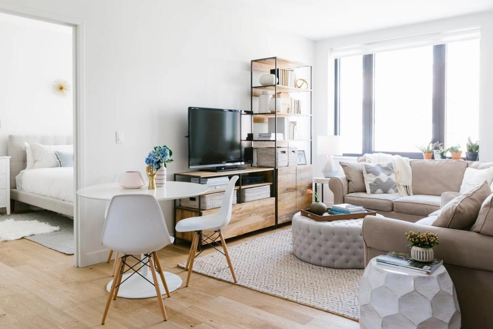 Mid-century modern small living room with TV on wooden stand, light neutral palette, natural wood legs on furniture, and bright airy aesthetic