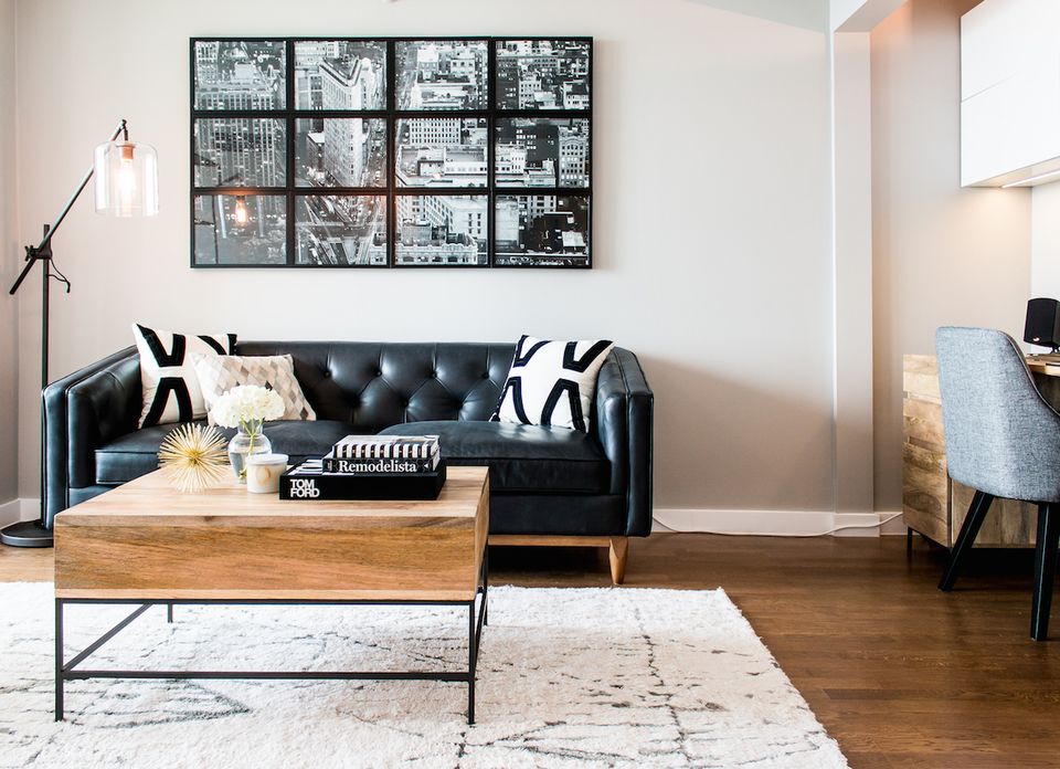 Modern living room with black leather sofa, geometric black and white pillows, natural wood coffee table, and gallery wall art