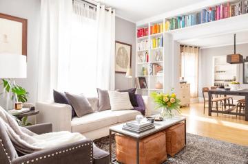 Transitional living room with neutral palette, colorful book wall, and multi-functional layout