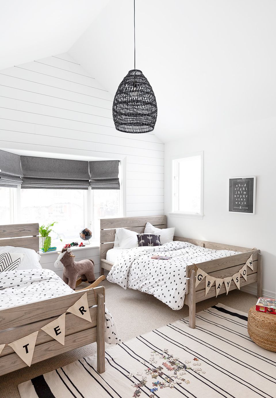 Scandinavian kids' bedroom with natural wood beds, woven pendant light, and striped carpet creating a bright, airy play space
