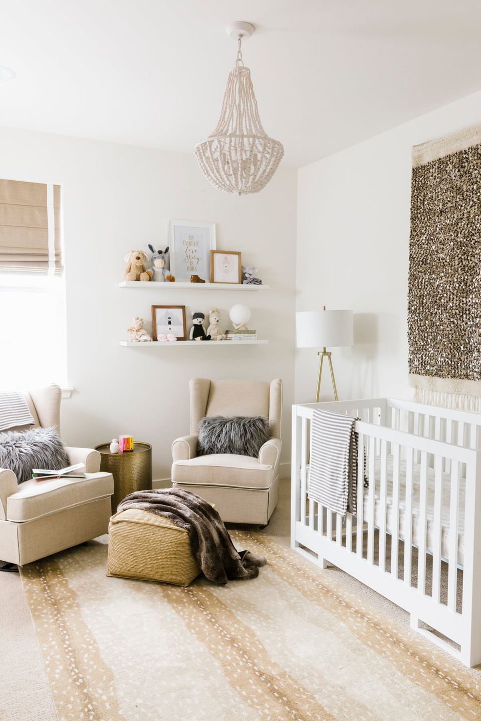 Modern neutral nursery with beaded chandelier, floating shelves, white crib, and curated accessories