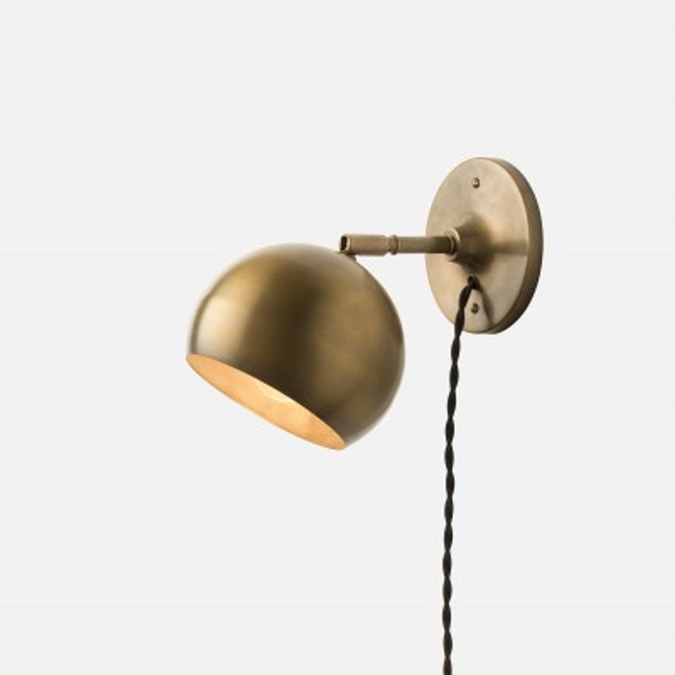 Mid-century modern brass plug-in wall sconce with dome shade and adjustable arm on neutral background