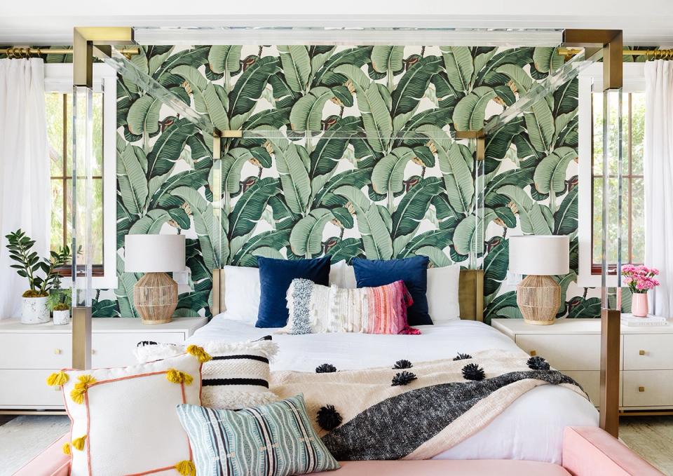 Tropical bedroom with bold banana leaf wallpaper, brass canopy bed, and colorful accent pillows