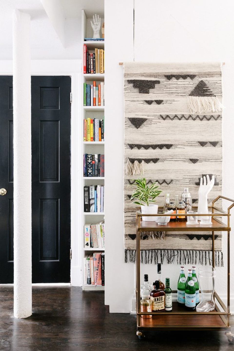 Minimalist boho workspace with geometric wall hanging, floating shelves, black door, and natural wood accents