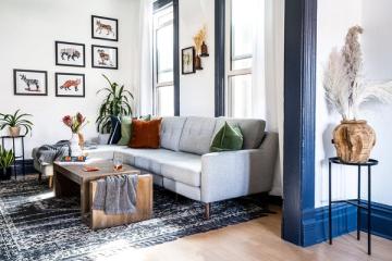 Modern living room with gallery wall art, light gray sofa, navy accent doors, and warm wood elements creating serene sophistication