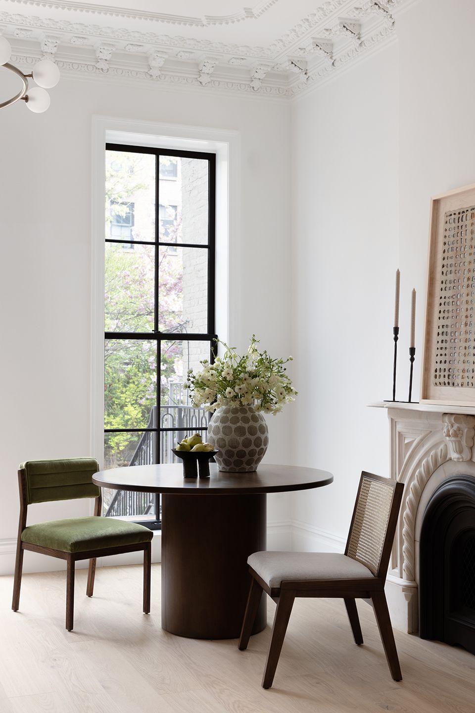 Contemporary round dining table with black wood base and olive green chairs by tall black-framed window