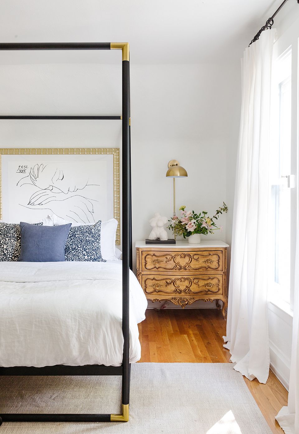 Contemporary bedroom featuring black metal four-poster bed, carved wood nightstand, and feminine palette