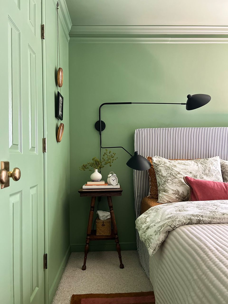 Soft sage green bedroom with striped headboard, black swing lamp, and cottage charm