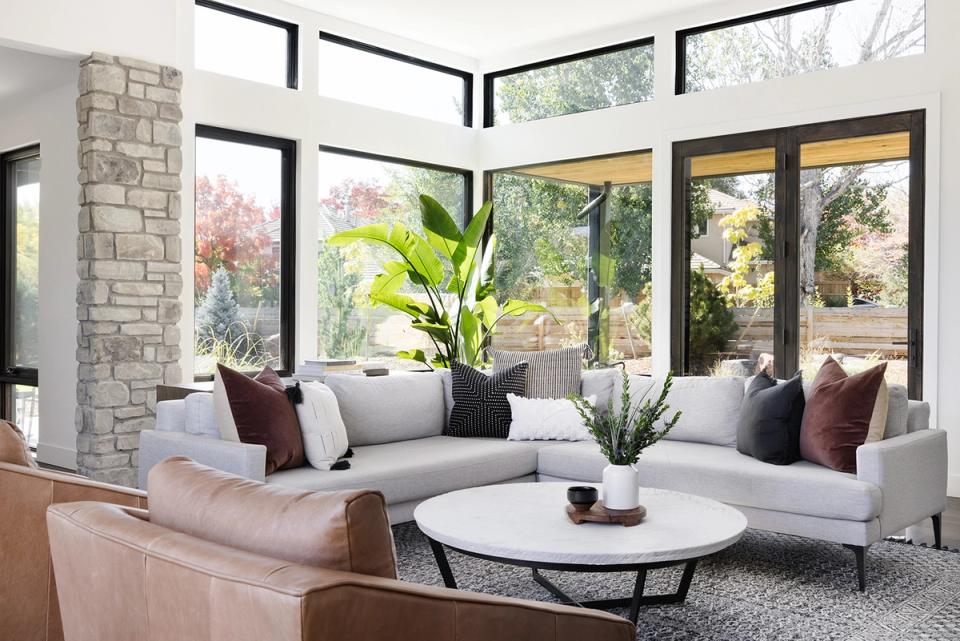 Modern living room with curved sectional, burgundy and gray pillows, stone fireplace and greenery