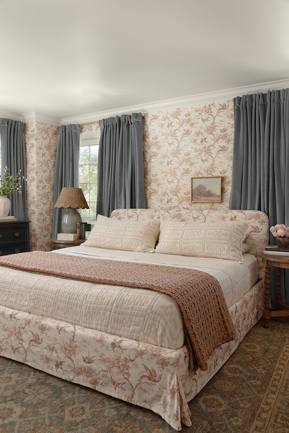 Romantic bedroom with rose toile wallpaper, gray drapes, and layered traditional textiles