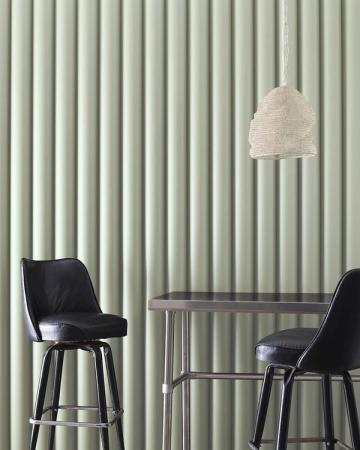 Minimalist sage green interior with vertical ribbed wall texture, black modern bar stools, and pendant lighting creating a calm, contemporary atmosphere