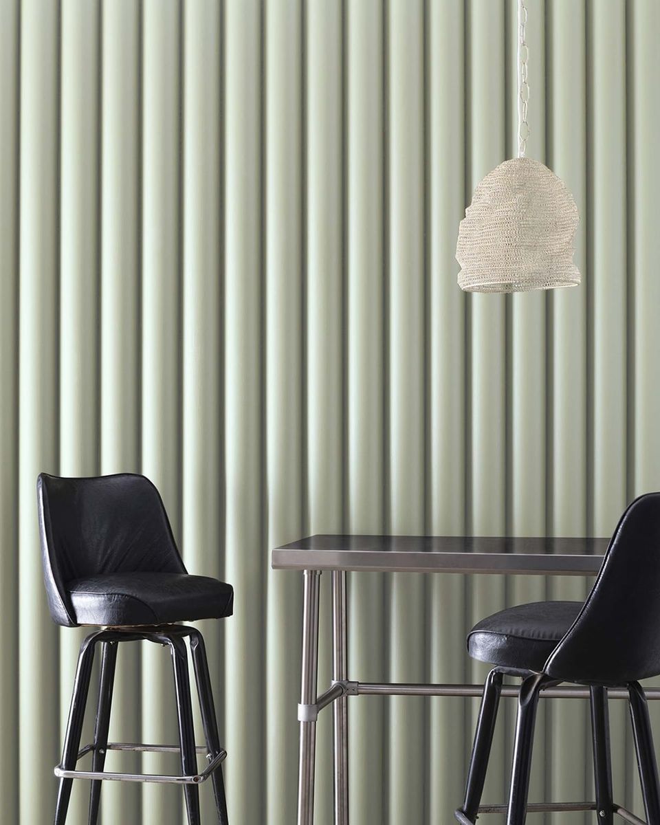 Minimalist sage green interior with vertical ribbed wall texture, black modern bar stools, and pendant lighting creating a calm, contemporary atmosphere