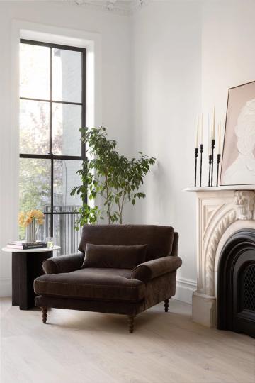 Minimalist modern living room with chocolate brown velvet chair, white walls, black-framed window, and fireplace mantel