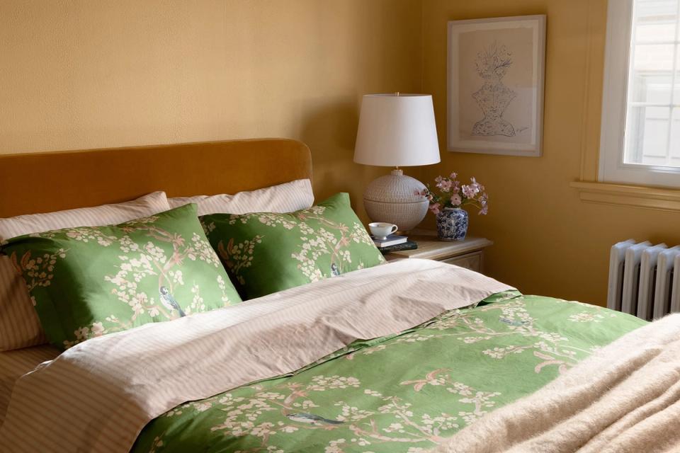 Warm golden bedroom with sage green botanical bedding and wood headboard