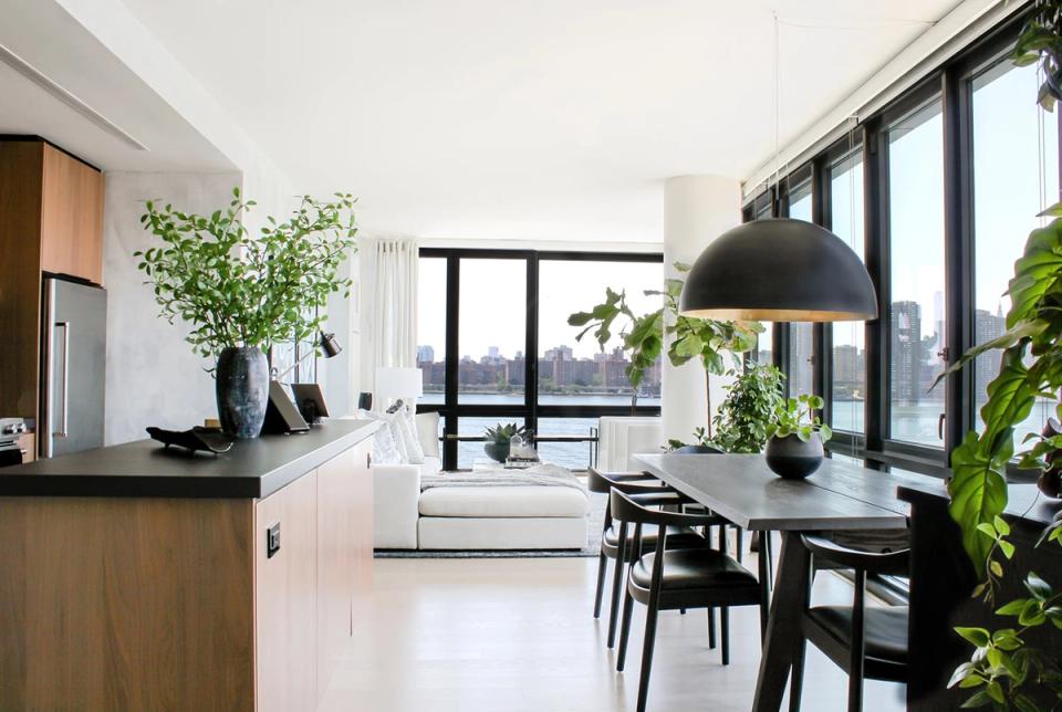 Contemporary open-concept dining and living area with abundant natural light, greenery, and black modern furnishings against white backdrop.