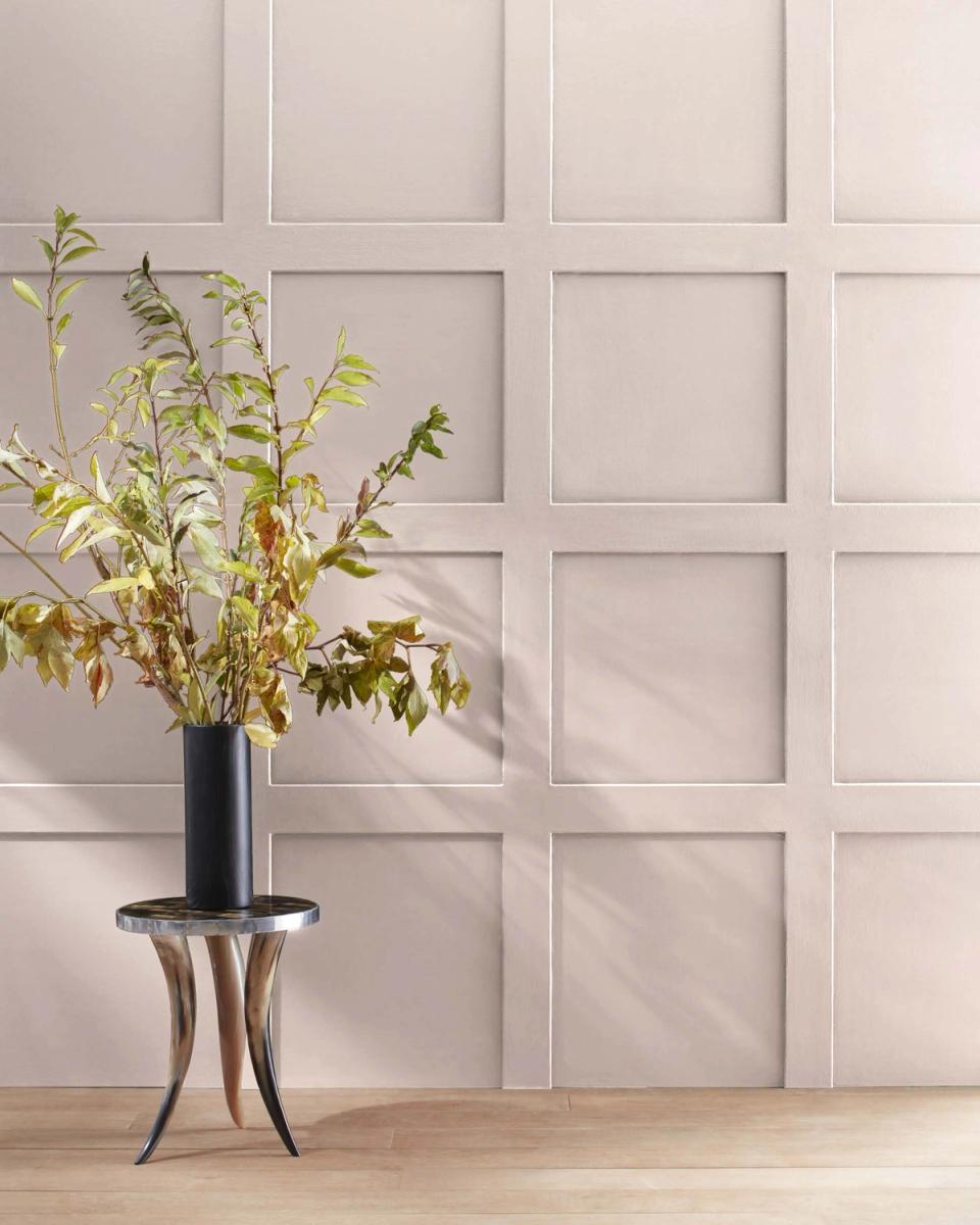 Soft mauve wall with geometric panel molding and fresh greenery in black vase on sculptural side table, modern organic aesthetic