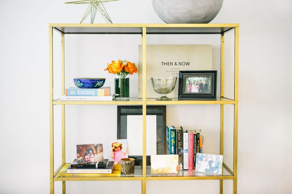 Contemporary brass shelving unit with minimalist styling: fresh flowers, ceramics, books, and curated accessories on clean white backdrop